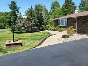 Front of brick home landscape bed with river rock, evergreen shrubs and slowering bordering walkway.