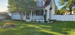 Beige home in suburbs with landscape bed with white decorative stone. Evergreen shrubs and flowering perennials surround the house on a sunny day.