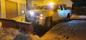 White plow truck removing snow from small parking lot on snowy night